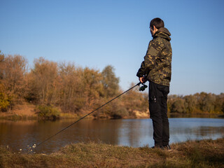 A young man is a fisherman with a spinning rod. Autumn fishing, outdoor activities and hobbies