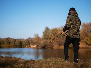 A young man is a fisherman with a spinning rod. Autumn fishing, outdoor activities and hobbies