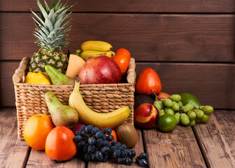 Mix of fresh juicy colorful exotic tropical fruits in basket on wooden background