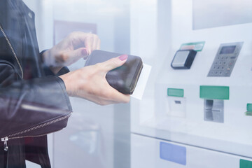 Female hand holds wallet and credit card on the background of ATM, withdraw cash money, Finance transactions