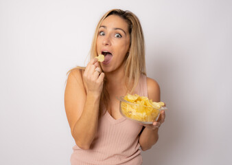 Young beautiful woman eating chips potatoes standing over white background very happy.