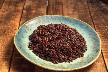Healthy food black rice in blue plate on wood table.