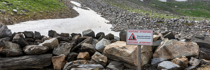 Fototapeta na wymiar Warning sign rockfall with text - Attention! Do not leave the path - english and german language. Panorama