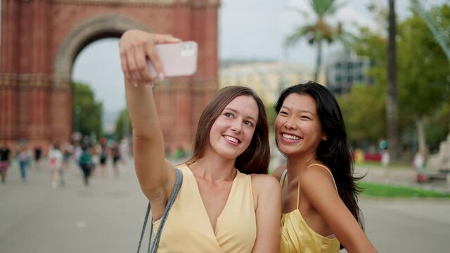 Smiling multiracial girlfriends tourists posing for selfie picture against historic building in city