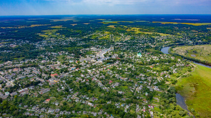 Aerial view of a small city on a beautiful summer day with a green landscape behind it. Picture from the drone of the village on a sunny day. Summer rural landscape from the top aerial view.