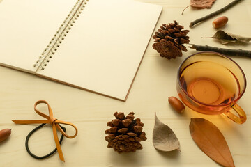 ノートとティーカップの周囲に秋の小物がちりばめられたイメージ