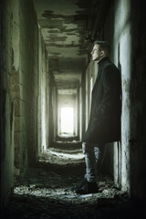 Young man with eyeglasses in dark ruined corridor vertical