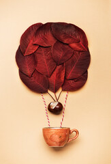 Colorful hot air balloon made of autumn leaves flying with a cup coffee on a beige background, top view. Creative minimal autumn idea