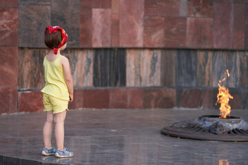 A little girl stands at the memorial with the eternal flame. Selective focus. Copy space.