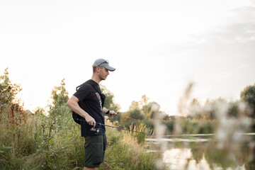 Happy young man fishing with a rod on the shore at sunset. fisherman smiling and waiting for the...