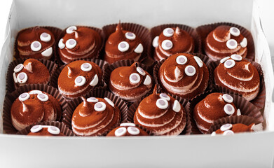 Set of cupcakes in the white gift box. Chocolate cupcake with brown whipped marshmallow top decorated with mastic smiley face and sprinkled with cocoa powder