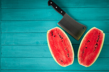 Watermelon sliced in a half with a backsword on the wooden turquoise background. Red juicy summer fruit berry
