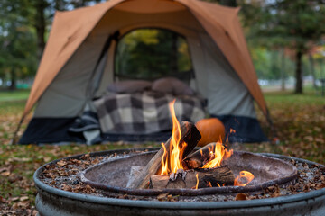 Closeup of campfire with orange tent in background - obrazy, fototapety, plakaty