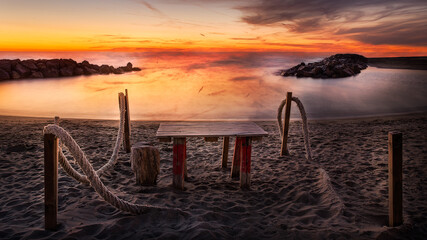 Naklejka na ściany i meble beach wooden table in a stunning sunset