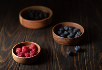 Berries of raspberries, blueberries and blackberries in wooden bowls on a dark background. Photo in a dark key