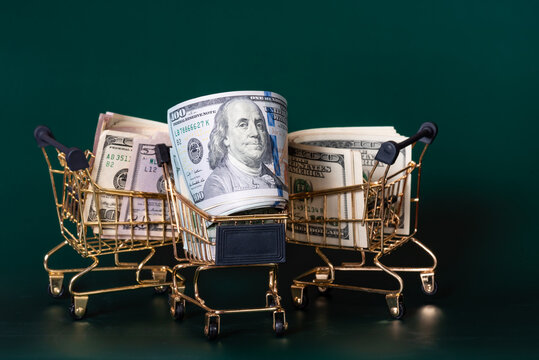 Three gold-colored grocery carts with dollars on dark green background. Banking and finance concept.
