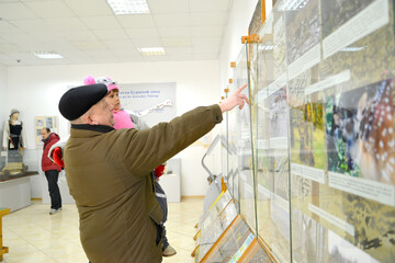 KALININGRAD REGION, RUSSIA. An elderly man shows his granddaughter photographs of animals in the nature hall. Museum Curonian Spit