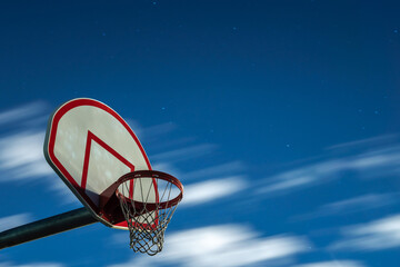 A long exposure photograph of a dirty orange and white playground basketball hoop, rim and net with...