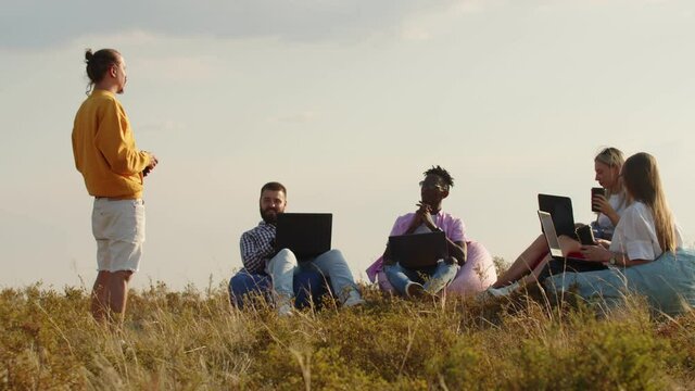 Field, four people are sitting in chair bags the grass with laptops their knees, listening to their coach. Concept of team building