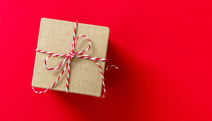 Christmas gift box on red color background. Red white striped string tied on brown kraft present.