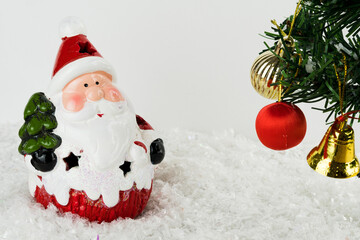 Table covered with snowflakes with Christmas decorations. Santa Claus, Christmas tree with red, gold balls and lights. Selective focus.