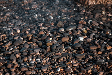 Pebbles on the seashore. Wet pebbles. The surf line. Sea foam. Close-up. Selective focus. Natural background.