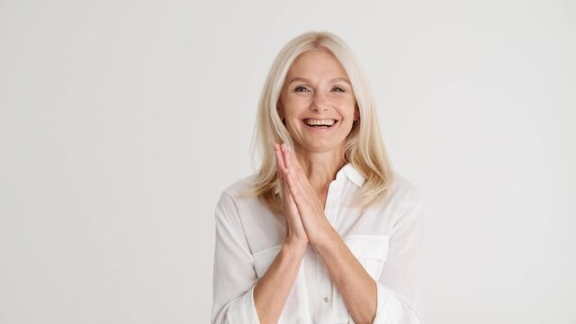 Positively surprised handsome mature woman clapping hands at the camera in the white studio
