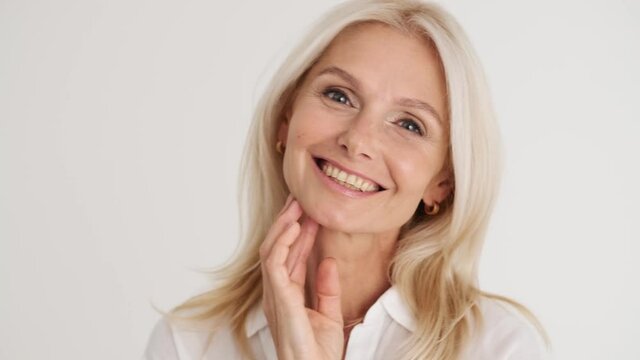 Close-up view of the smiling mature woman posing at the camera in the white studio