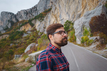 Naklejka premium Male hipster Traveler with backpack in plaid shirt and jeans hiking in the mountains travel, trekking in autumn countryside, road in the mountains