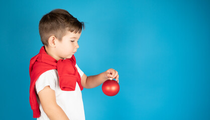 Fototapeta na wymiar Child holding red Christmas bauble over blue background with copy space. Christmas dreams or wishes concept