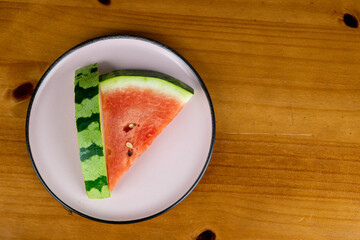 delicious slices of red watermelon served in light plate on table with wooden background, photo view from above.