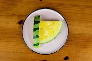 delicious slices of yellow watermelon served in light plate on table with wooden background, photo view from above.