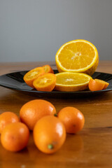 small oranges on the wooden table in the dark black background with cut oranges, close-up photo.