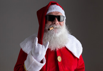 Santa Claus wearing sunglasses showing the rocker hand sign and smoking a cigar on dark background