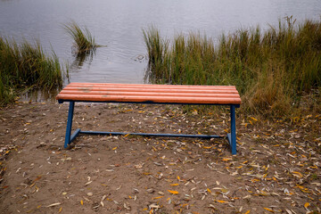 A park bench sits empty by the shore of a lake in the fall, bench at the lake