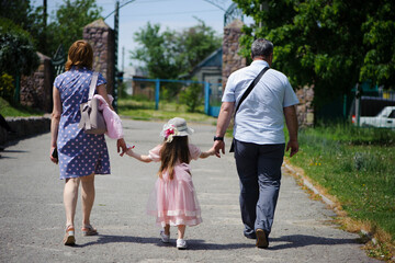 family walking in the park. mom dad and little girl walking holding hands. back view. daughter in a pink dress. friendly loving family concept, love. outdoor, walk in the fresh air, threesome