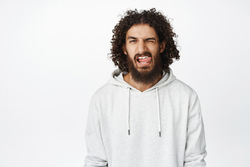 Sassy and cool middle easter man winking, showing tongue, macho face expression, standing in hoodie over white background