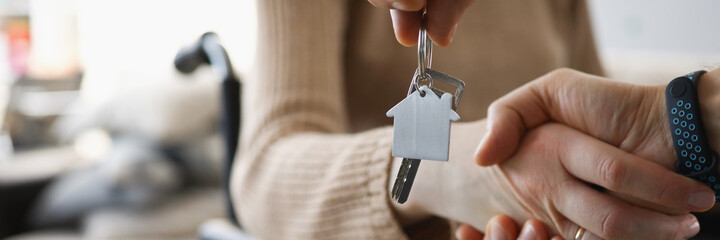 Disabled woman in wheelchair shaking hands with man with keys to new apartment closeup