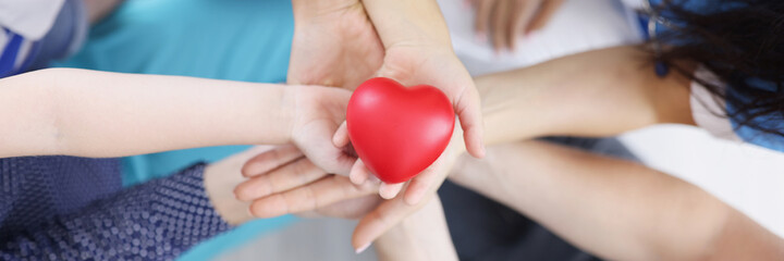 Many adults and children hands are holding plastic toy heart top view