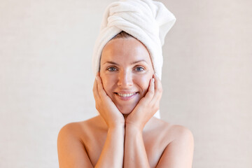 Closeup portrait of beautiful young woman with towel on head. Beautiful girl after bath touching her face. Skincare concept