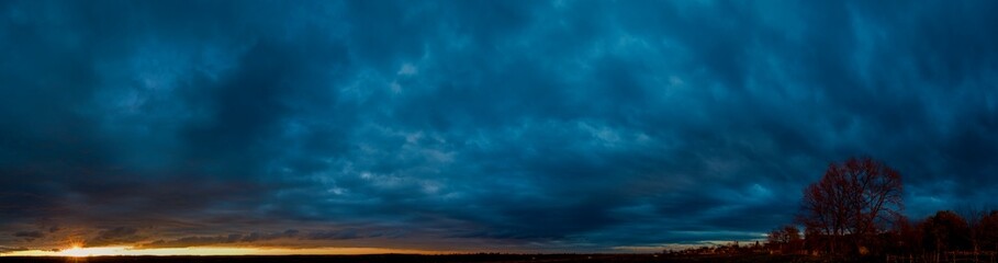 Panorama of dawn fire in the sky above the natural pasture. Golden red clouds just before sunrise. Picturesque landscape at sunrise. Beauty in nature