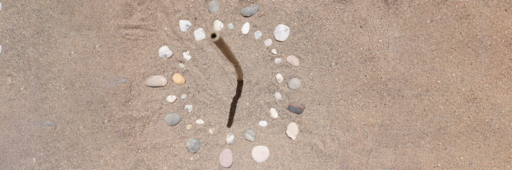 Sundial is lined with stones on sand of sea beach closeup background