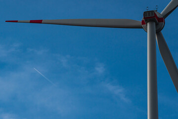 A windmill in front of a blue sky with a plane which is flying 