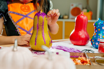 Little girl in whitch costume painting pumpkins at home