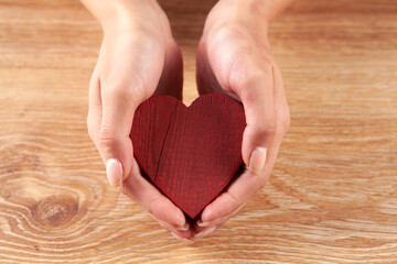 female hand holding red wooden heart, love, care concept