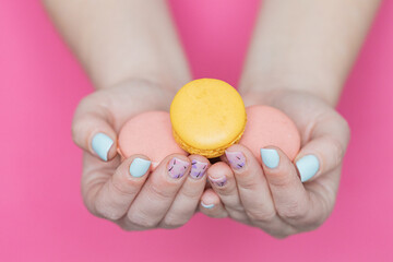 woman's hands with nails painted with macarrons on a pink background 