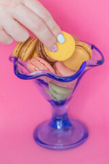 woman's hand with painted nails taking a macaron from a bowl on a pink background