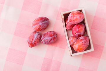 Fresh organic purple plums on a pink textile background. Ripe fruit with a wooden container on the tablecloth