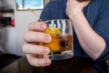 Close up of a causcasian male hand holding an old fashioned alcoholic drink inside of a bar and restaurant