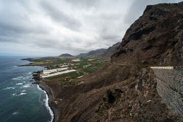 Rocky coast of the Atlantic Ocean. In the background, the small town of Buenavista del Norte. View from the observation deck - Mirador Punta del Fraile. Tenerife. Canary Islands. Spain.
